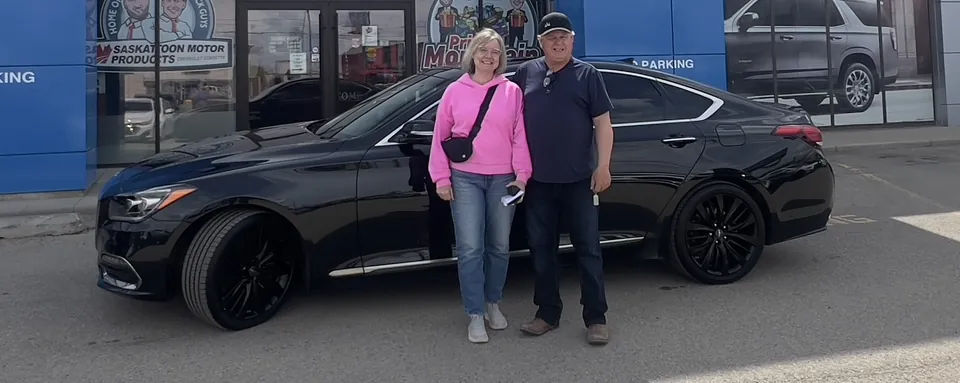 Two people beside a black sedan outside the dealership