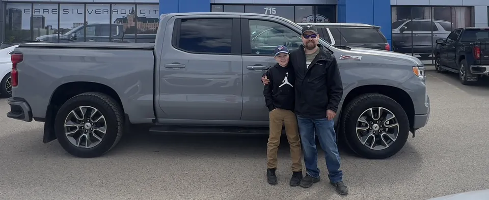 Two people beside a silver pickup at the dealership