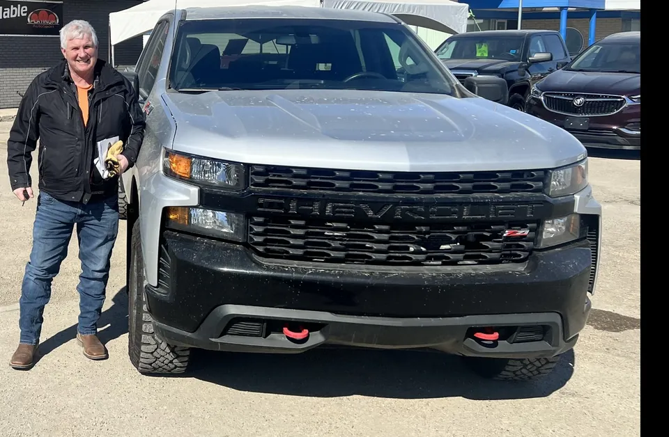 A person beside a silver pickup in the vehicle lot