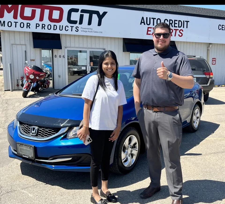 Two people beside a blue sedan outside the dealership