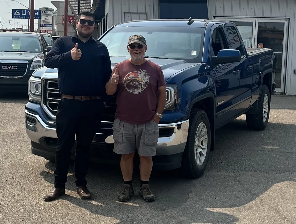 Two people beside a blue pickup outside the dealership