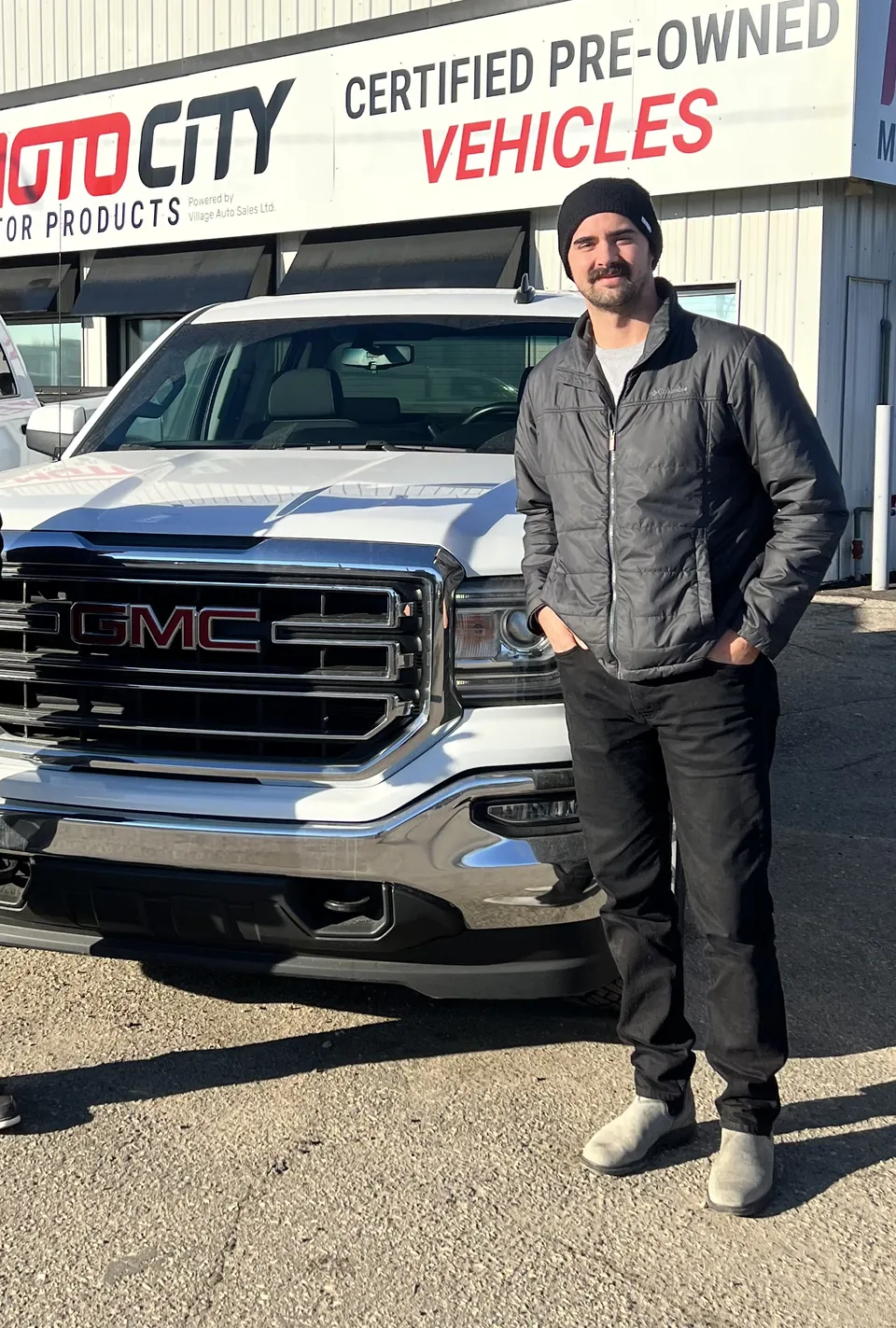 A person beside a dark pickup outside the dealership