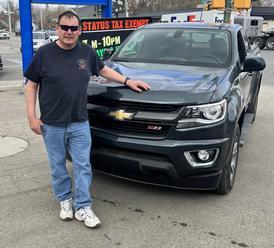 A person beside a dark pickup in the vehicle lot