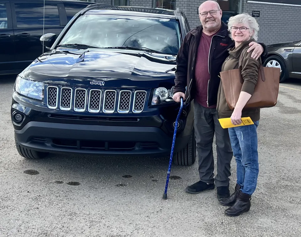Two people beside a dark blue SUV in the vehicle lot