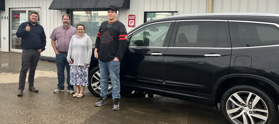 Four people beside a black SUV outside the dealership