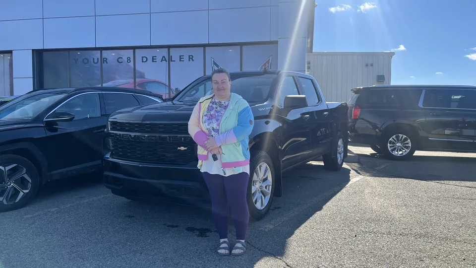 A person beside a dark pickup in front of the dealership