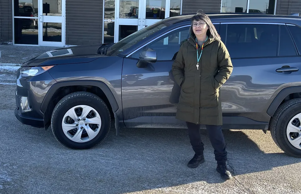 A person beside a grey SUV outside the dealership