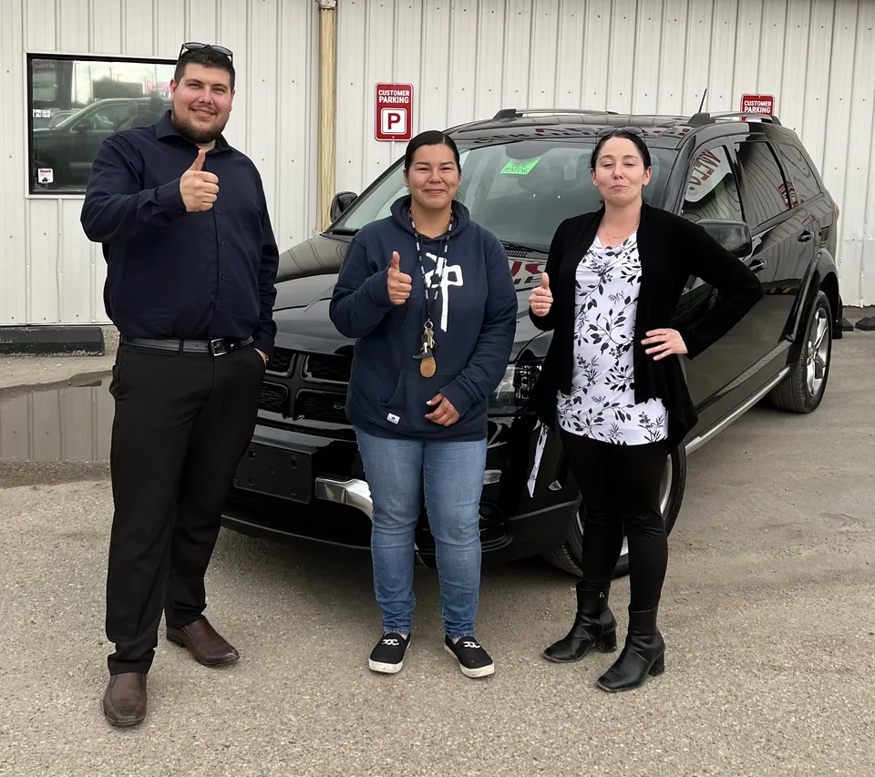 Three people beside a dark SUV outside the dealership