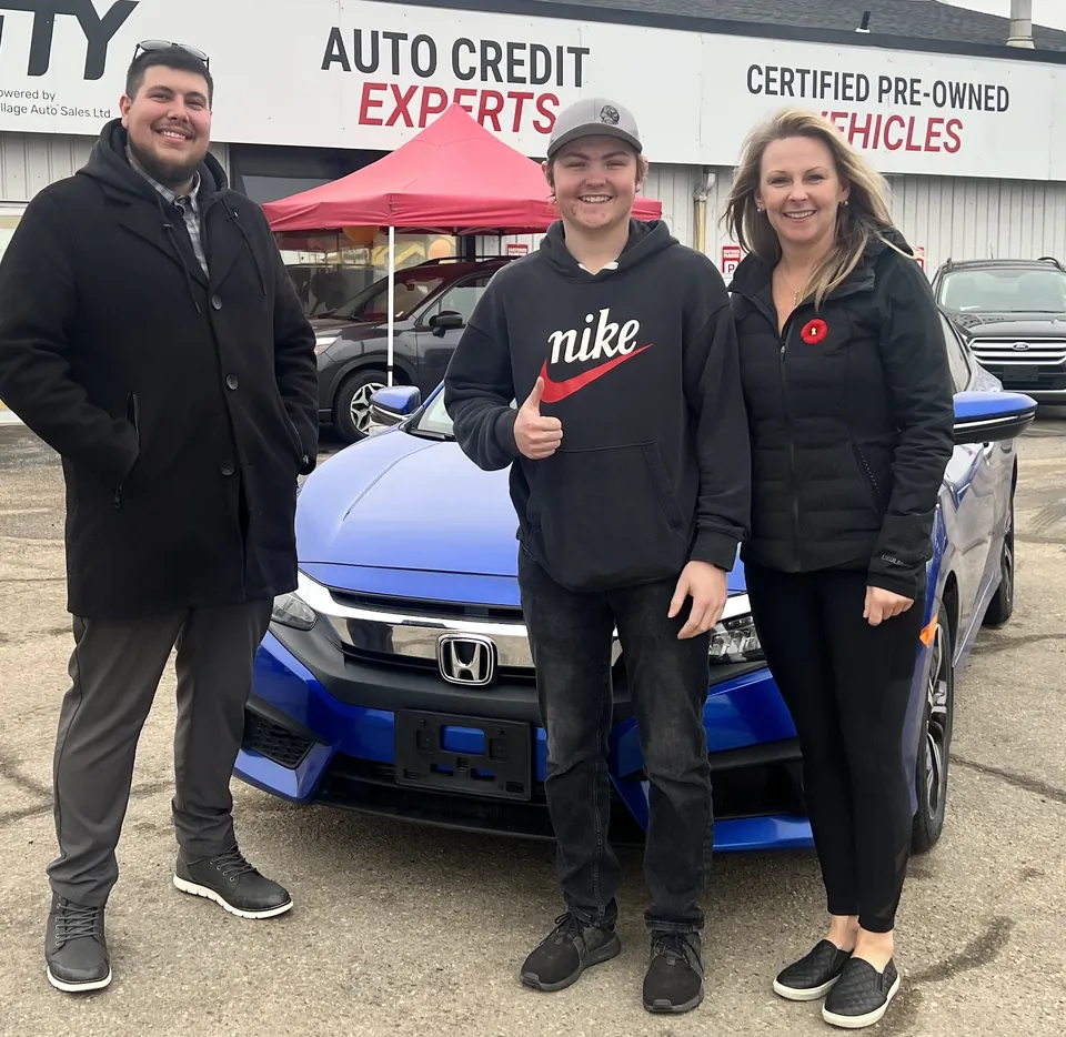 Three people beside a blue car outside the dealership
