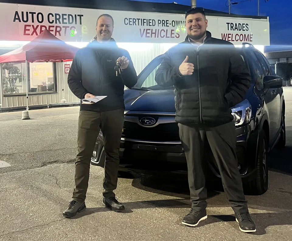 Two people beside a dark SUV outside the dealership