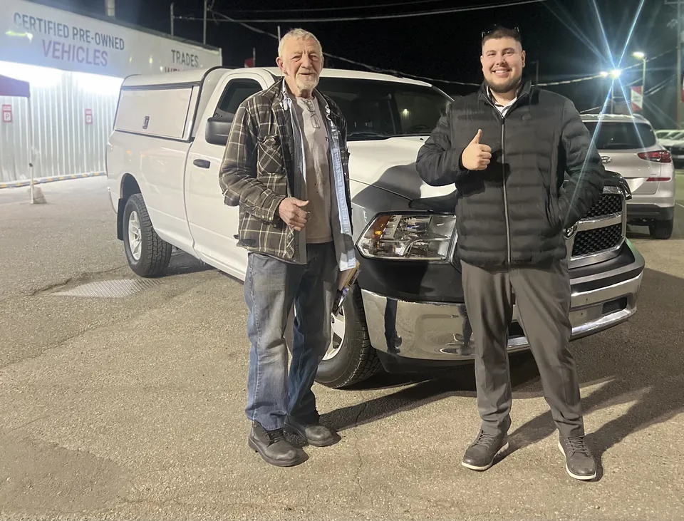 Two people beside a white pickup outside the dealership at night