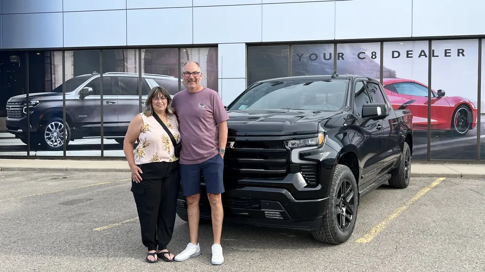 Two people beside a black pickup outside the dealership