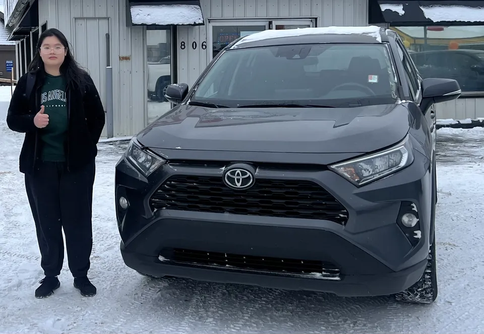 A person beside a grey SUV in the vehicle lot