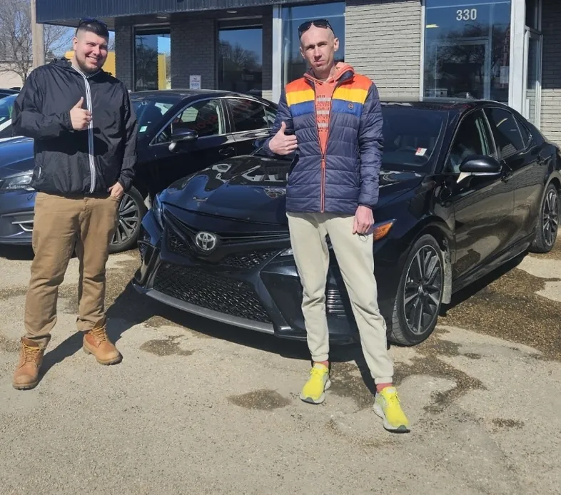 Two people beside a black sedan outside the dealership